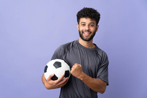 Handsome Moroccan young football player man over isolated on purple background celebrating a victory - Фото, изображение