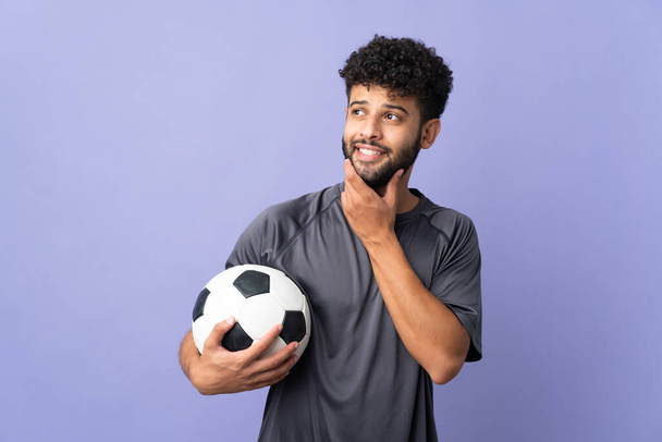 Όμορφος Μαροκινός νεαρός ποδοσφαιριστής απομονωμένος σε μωβ φόντο κοιτώντας ψηλά χαμογελώντας. - Φωτογραφία, εικόνα