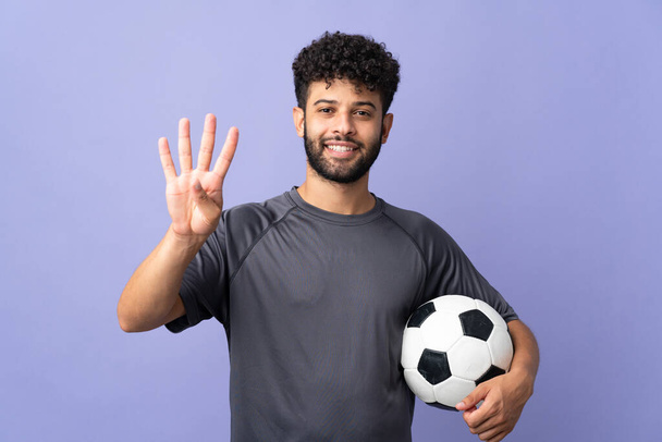 Handsome Moroccan young football player man over isolated on purple background happy and counting four with fingers - Photo, image