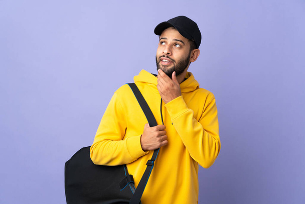 Young sport Moroccan man with sport bag isolated on purple background looking up while smiling - Photo, image