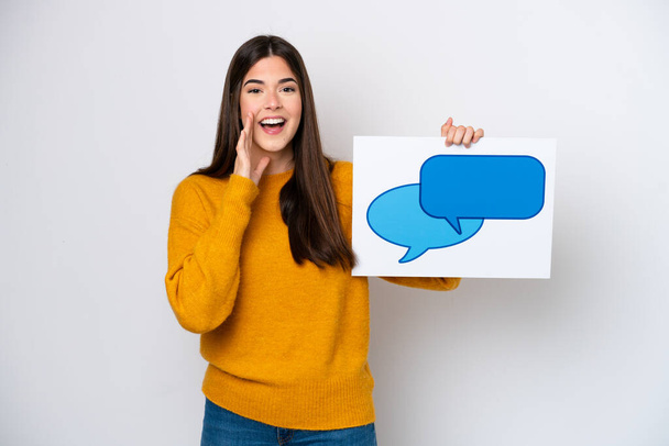 Young Brazilian woman isolated on white background holding a placard with speech bubble icon and shouting - Photo, Image