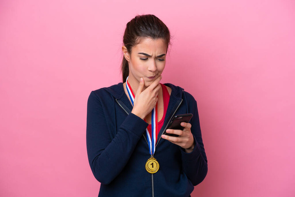 Joven deportista brasileña con medallas aisladas sobre fondo rosa pensando y enviando un mensaje - Foto, Imagen