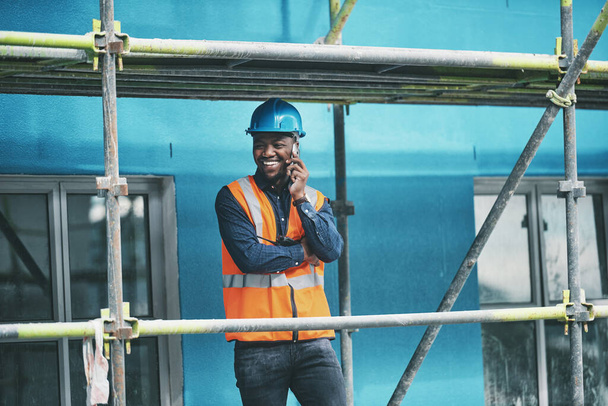 We gingen op de goede weg. Foto van een jongeman aan het praten op een mobiele telefoon tijdens het werken op een bouwplaats. - Foto, afbeelding