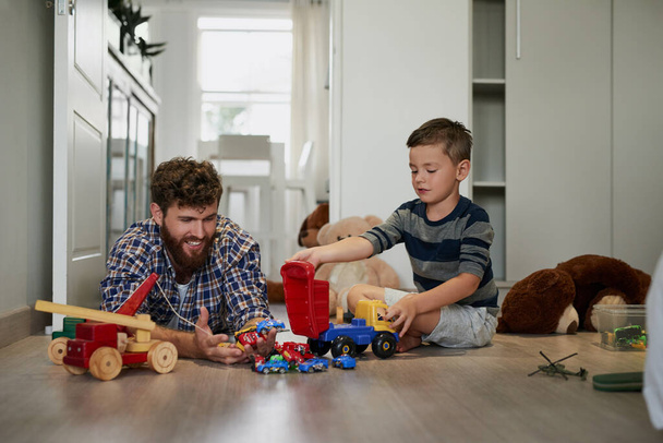Jungen und ihr Spielzeug. Aufnahme eines hübschen jungen Mannes und seines Sohnes beim Spielen mit Spielzeug auf dem Schlafzimmerboden. - Foto, Bild