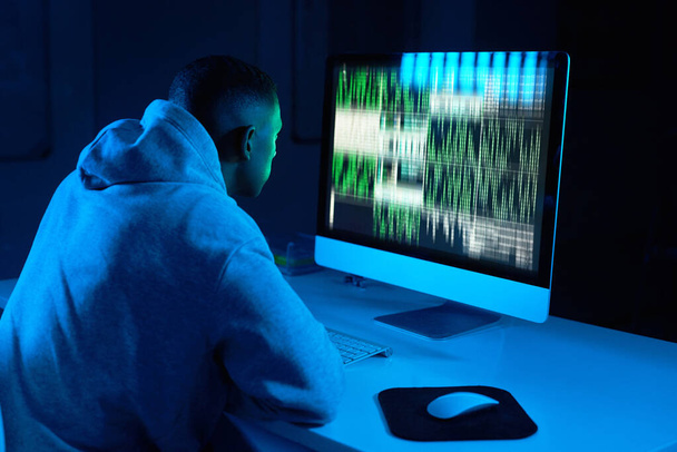 Hes always sticking to the code. Shot of a young male hacker cracking a computer code in the dark. - Photo, Image