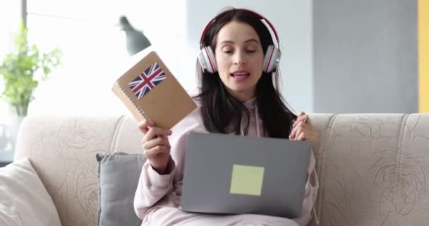 Woman in headphones is learning British English remotely on laptop - Filmmaterial, Video