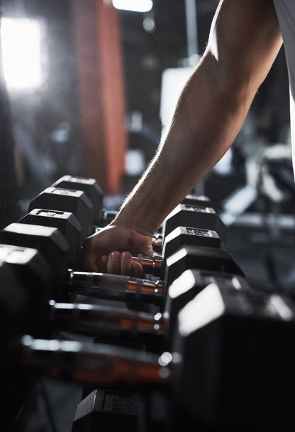 Lets grab a heavier weight. Cropped shot of an unrecognizable male athlete grabbing a set of dumbbells during his workout in the gym. - 写真・画像