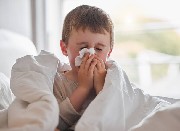 Mijn neus blijft maar druppelen. Schot van een kleine jongen die zich ziek voelt in bed thuis en snuit zijn neus. - Foto, afbeelding