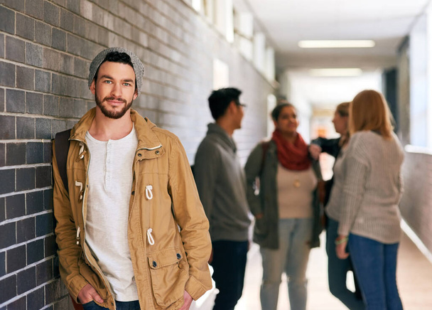 Kampüsteki havalı adam. Arka planda sınıf arkadaşlarıyla kampüs koridorunda duran genç bir üniversite öğrencisinin portresi.. - Fotoğraf, Görsel