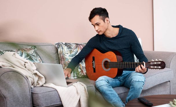 What lessons has lockdown taught you. Shot of a young man using a laptop while playing the guitar at home. - Foto, Bild