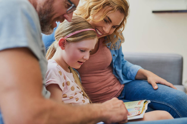 Her reading skills are improving thanks to her parents. Cropped shot of a mother and father reading a book with their daughter on the sofa at home. - 写真・画像