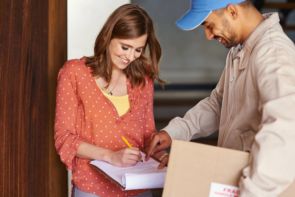 Just sign right there. Cropped shot of an attractive young woman signing for her delivery. - 写真・画像