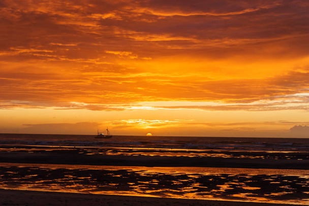 Όμορφο ηλιοβασίλεμα με δραματικό μουντό συννεφιασμένο ουρανό πάνω από τον ωκεανό της Βόρειας Θάλασσας και σιλουέτα ενός πλοίου, De Haan, Βέλγιο. - Φωτογραφία, εικόνα
