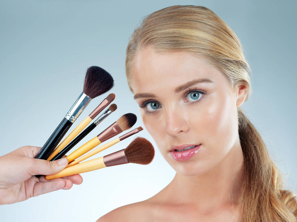 Studio portret van een mooie jonge vrouw poseren met make-up borstels tegen een blauwe achtergrond. - Foto, afbeelding