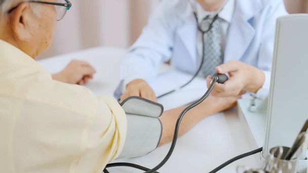 Aziatische senior patiënt heeft medisch onderzoek met een arts in het ziekenhuis. Dokter past bloeddrukmeter aan op oudere grijze man - Foto, afbeelding