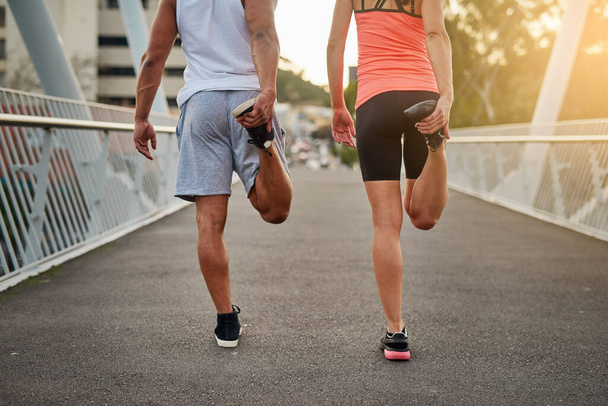 Getting their legs ready for a run. Rearview shot of a young couple warming up on a bridge before their workout. - Photo, Image