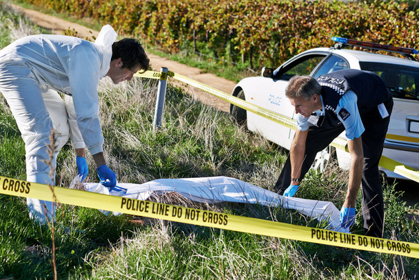 Covering the body. Shot of two investigators picking up a body bag at a crime scene. - Photo, image