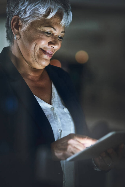 Trabajo duro apoyado por la tecnología inteligente. Fotografía de una mujer de negocios madura usando una tableta digital tarde en la noche en una oficina moderna. - Foto, imagen