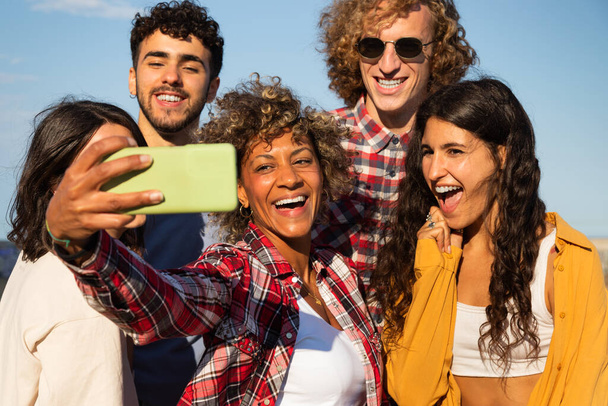 Усміхнені молоді багаторасові друзі беруть селфі разом, використовуючи смартфон на відкритому повітрі
 - Фото, зображення