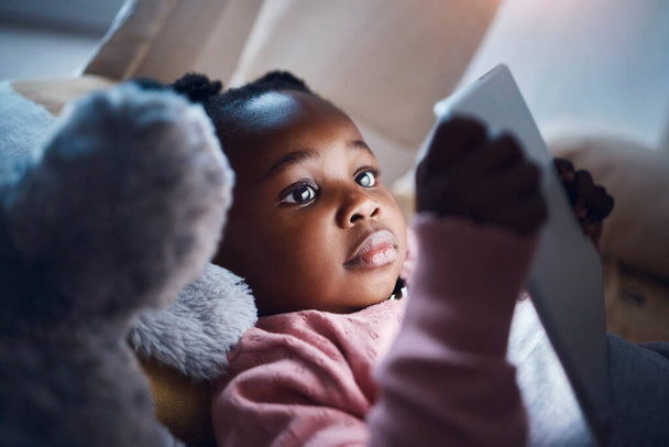 Im glad mom lets me read in bed. Shot of a little girl using her digital tablet in her bedroom. - Foto, Imagen
