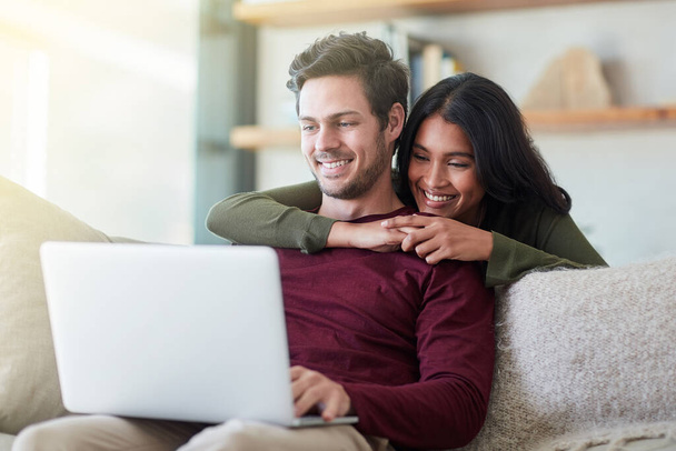 En lo que estás trabajando. Foto de una pareja joven y cariñosa usando su computadora portátil mientras se relaja en el sofá en casa. - Foto, imagen