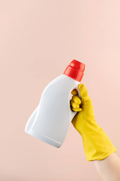 A mockup of a bottle of laundry gel in a yellow rubber glove on a pink. - Fotoğraf, Görsel