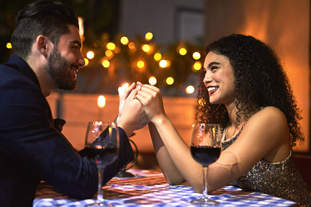 Wir werden für immer zusammenbleiben. Aufnahme eines fröhlichen jungen Paares, das sich Händchen hält, während es sich bei einem Dinner bei Kerzenschein in die Augen blickt. - Foto, Bild