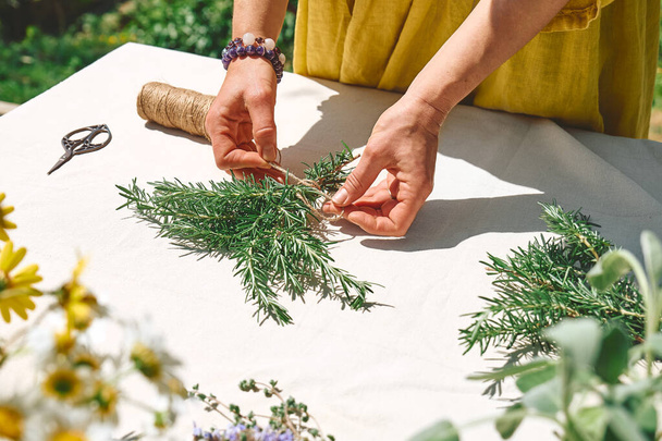 Alternative medicine. Collection and drying of herbs. Woman holding in her hands a bunch of rosemary. Herbalist woman preparing fresh scented organic herbs for natural herbal methods of treatment. - Foto, Imagen