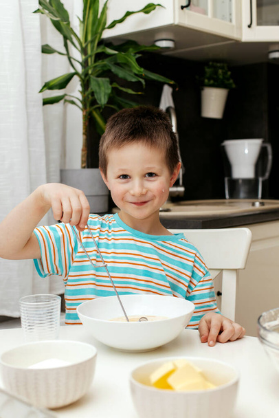 A little boy kneads the dough with a whisk and tastes it. The children are baking a cake. Little chef and helper - Foto, Imagem
