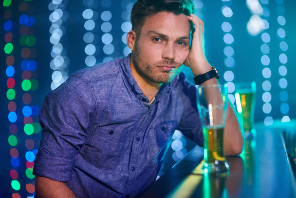 Here to drink all my sorrows away. Portrait of a young man looking upset while sitting at the bar in a club. - Photo, Image
