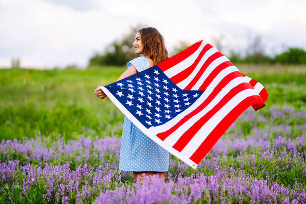 Young woman proudly hold waving american USA flag on blooming meadow.  4th of July. Fourth of July. Freedom. Patriotic holiday. Independence Day. - Photo, image