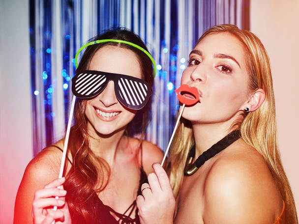 TGIF. Shot of two beautiful young women having fun with props in a photobooth. - Photo, Image