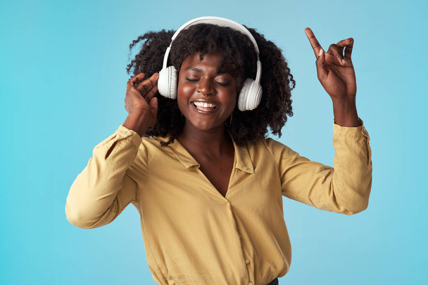 Life is beautiful, live it up. Studio shot of a young woman using headphones and dancing against a blue background. - Foto, Bild