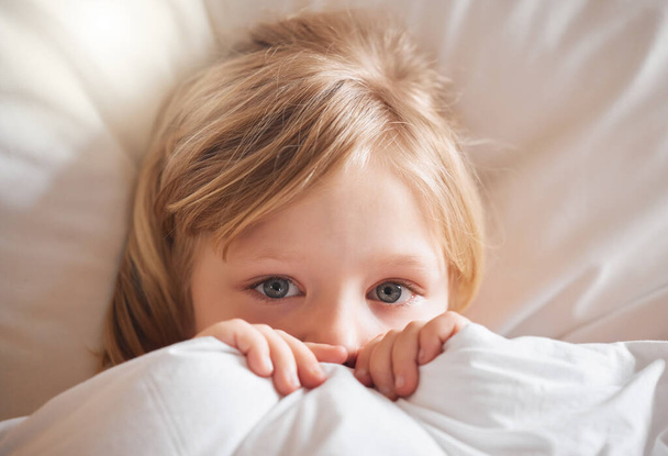 Δεν αισθάνομαι καθόλου καλά. Πυροβολισμός ενός μικρού κοριτσιού που νιώθει άρρωστη στο κρεβάτι και σκεπάζεται με μια κουβέρτα.. - Φωτογραφία, εικόνα