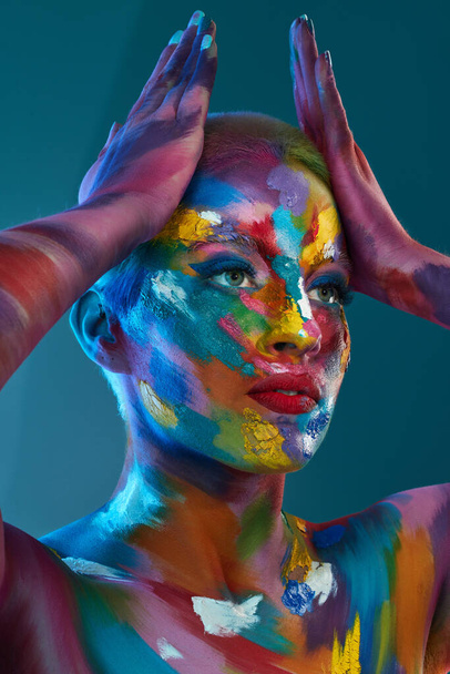 De kleuren die we zien en gebruiken zijn niets minder dan magisch. Studio shot van een jonge vrouw poseren met multi-gekleurde verf op haar gezicht. - Foto, afbeelding
