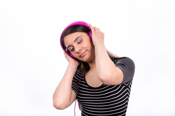 Portrait of beautiful smiling girl with long hair. The young woman wears jeans and a striped shirt and uses headphones to listen to music. - Zdjęcie, obraz