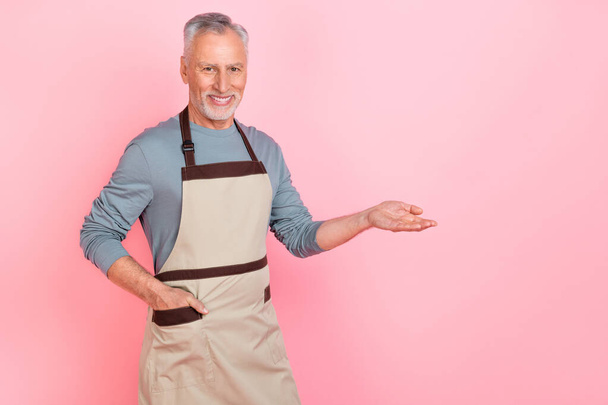 Photo of confident cute retired man wear grey shirt apron holding arm empty space isolated pink color background - Foto, Bild