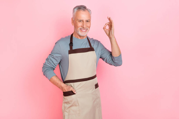 Photo of sweet pretty man pensioner dressed grey shirt apron showing okey sign isolated pink color background - Fotografie, Obrázek