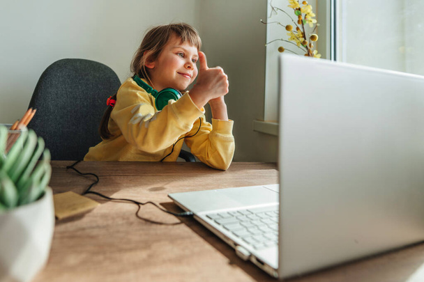 Schöne kleine 5-jährige Mädchen mit Laptop sitzt am Tisch im Zimmer. Online-Bildungskonzept. Kommunikation online, Videochat. Familie mit Technologie zu Hause. Selektiver Fokus. - Foto, Bild