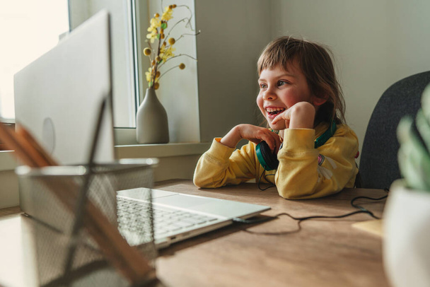 Beautiful little 5 years old girl using laptop sitting at the table in the room. Online education concept. Communication online, video chat. Family using technology at home. Selective focus. - 写真・画像