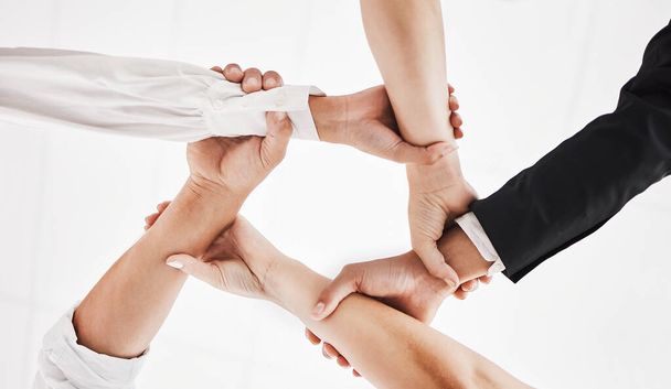 None of us is as strong as all of us. Low angle shot of a group of businesspeople holding one anothers wrists in a circular formation. - Foto, imagen