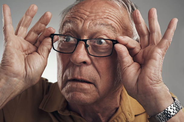 Cant believe what I just saw. Studio shot of an elderly man adjusting his spectacles against a grey background. - Foto, immagini