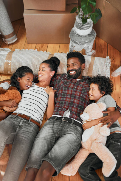 Iedereen lijkt van het nieuwe huis te houden. Shot van een gezin van vier liggend samen op de vloer in hun nieuwe huis. - Foto, afbeelding
