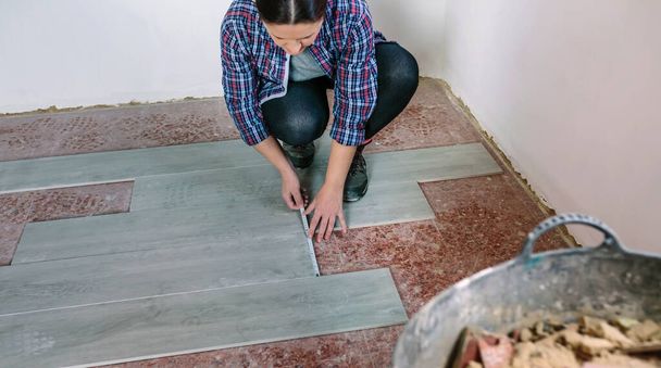 Female bricklayer measuring tiles to install a floor - Фото, изображение