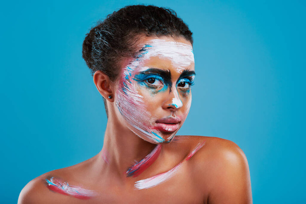 Jasná, odvážná a krásná. Studio portrét krásné mladé ženy pokryté obličejovou malbou pózující na modrém pozadí. - Fotografie, Obrázek