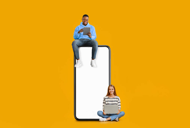 Ζευγάρι κάθεται σε λευκή άδεια οθόνη smartphone και χρησιμοποιώντας gadgets - Φωτογραφία, εικόνα