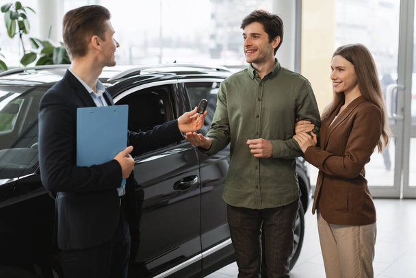 Positivo auto showroom manager dando auto chiave per felici giovani clienti presso concessionaria auto - Foto, immagini