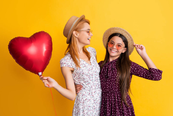 positive mom and daughter hold love heart balloon on yellow background - Foto, afbeelding