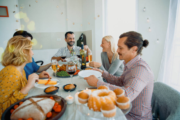Веселые Мультиэтнические друзья, празднующие Праздник вместе с едой и смехом. Семья собирается за кухонным столом в День Благодарения - Фото, изображение