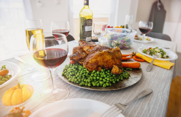 Жареная курица, бобы и морковь на большой тарелке подаются на большой ужин за обеденным столом с вином. - Фото, изображение